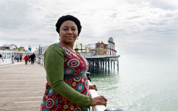 Awa Gaye Jeng, Article 26 Scholar, standing on the Palace Pier with the stripy helter skelter behind her
