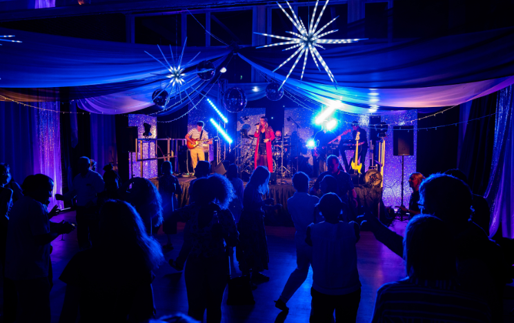 Figures on the dancefloor with band playing in background, lead singer Helen Nagle wears red long jacket