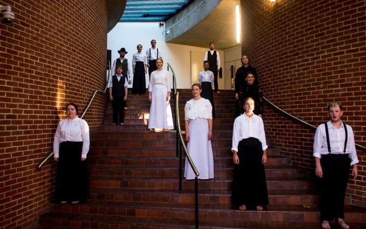 Corinne Furman and fellow drama students wearing black and white, standing on different stairs in the Attenborough Centre