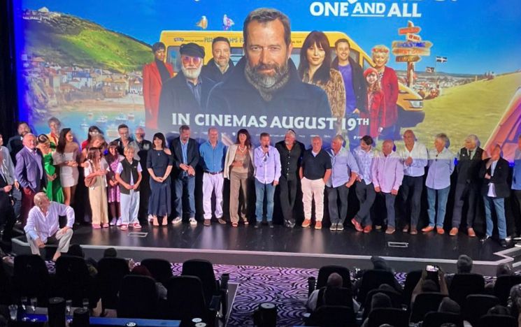 Alumna Corinne Furman and the cast of Fisherman's Friends: One and All standing on a stage with film advert backdrop