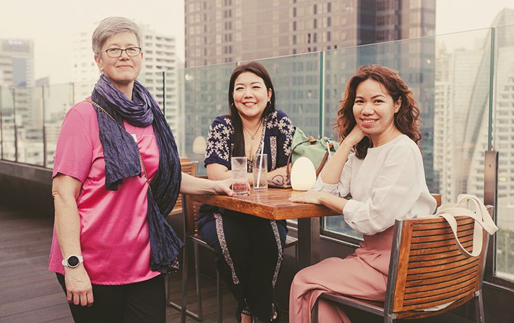 Sasha Roseneil stands next to two seated alumnae in Bangkok