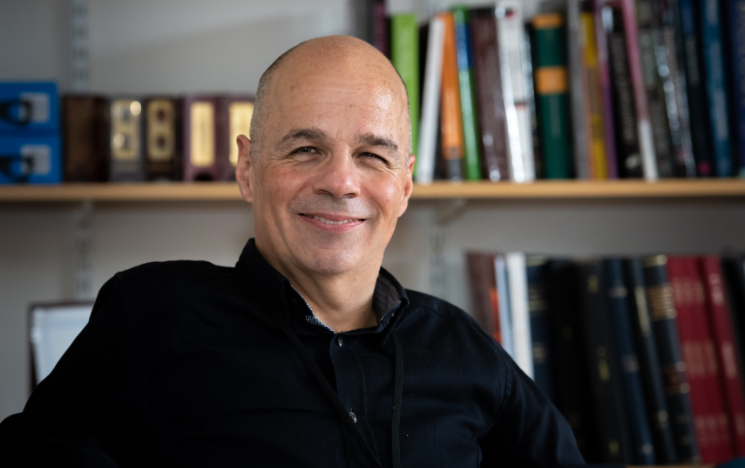 Professor David Ruebain sat in front of two sets of bookshelves smiling.