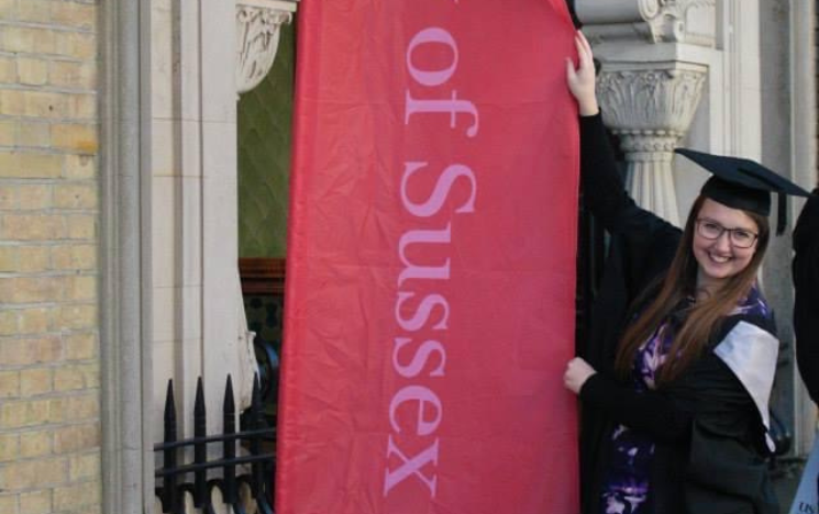 Jodie holding onto a red University of Sussex banner in her graduation gown.