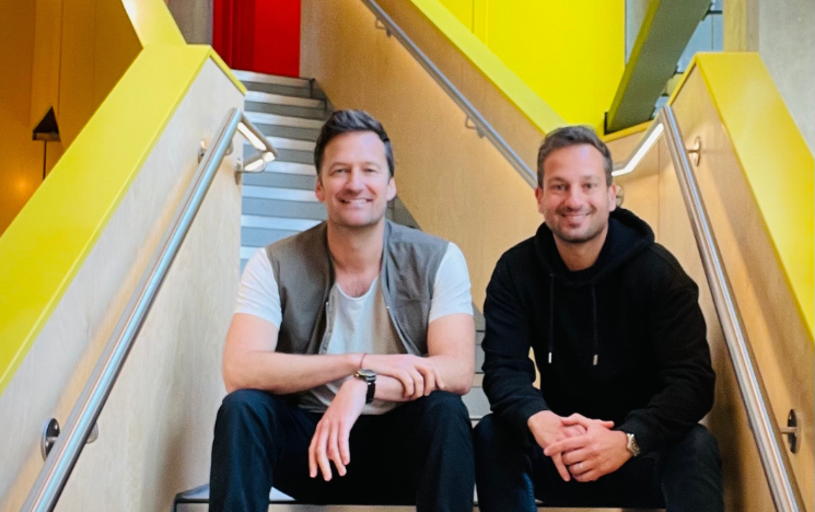 David Parr and Omid Moallemi sat together on a flight of stairs, smiling.