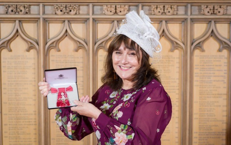 Elaine Bousfield holding up her MBE at Windsor Castle.
