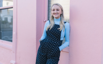 Millie Gooch stood smiling to the camera, as she leans against a pink wall.