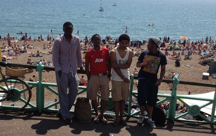 Seun Fasoranti standing with 3 friends on the Brighton Promenade in front of Brighton Beach.