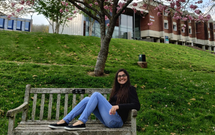 Student sitting on a bench in front of cherry trees and a building on campus