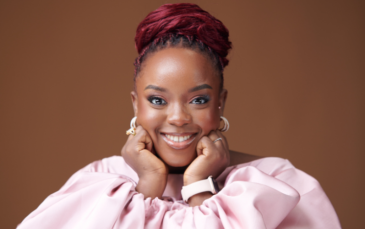 Portrait of Jennifer Uchendu smiling at the camera with her hands resting under her cheeks.