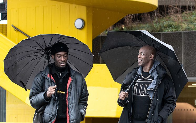 Topher Campbell and Jordi Carter talking to each other, walking in the rain outside the South Bank Centre