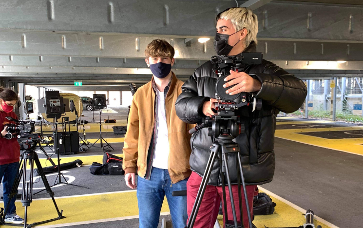 Pablo Santana stood behind a camera with a fellow student in a cark park.