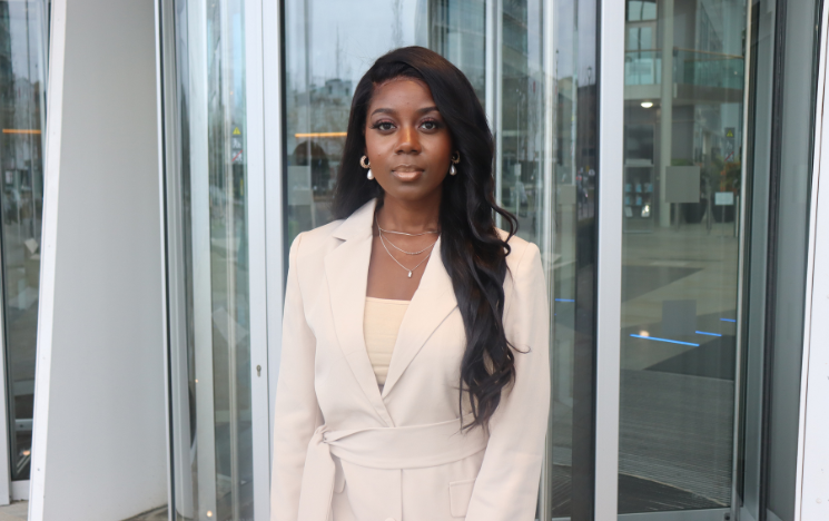 Lakeisha Annang in a smart, white coat standing in front of revolving doors.