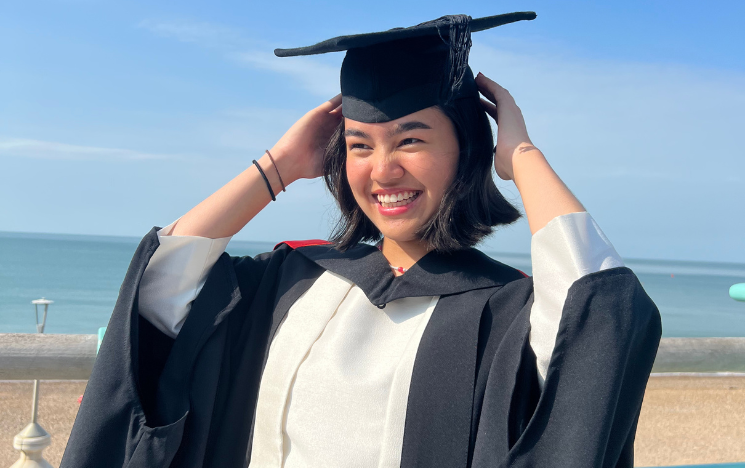 Rachel Nielsen smiling in her graduation gown on Brighton Beach.