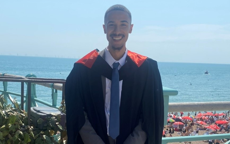 Marley Ahmed stood in front of Brighton and Hove beach in his graduation gown.