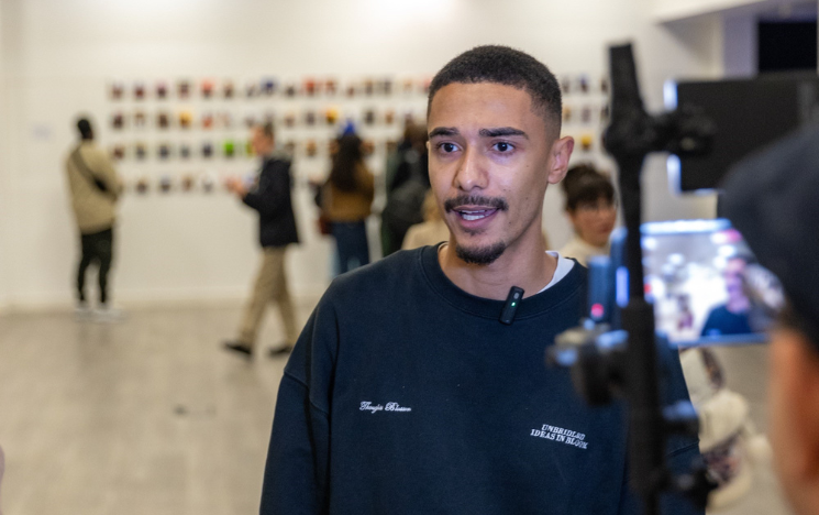 Marley Ahmed being filmed by a video camera with a gallery blurred out in the background.