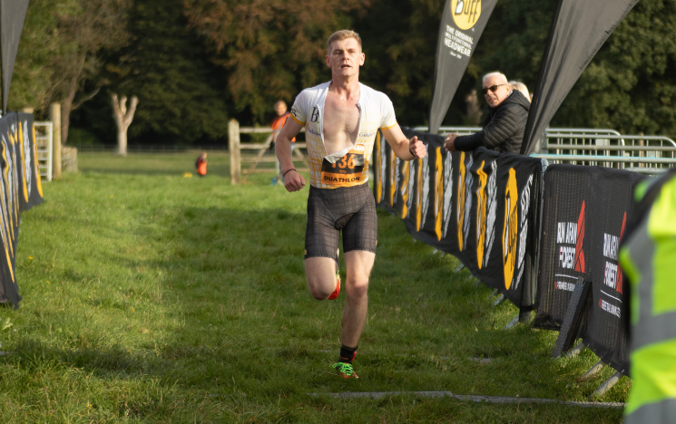 Olly Watts running in a duathlon while spectators look on.
