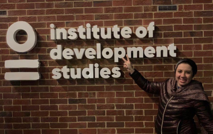 Amira Saber holding up her hand in front of the Institute of Development Studies sign.