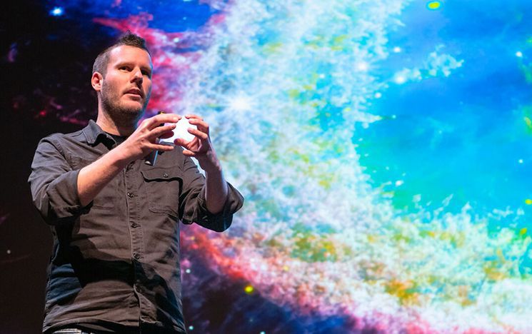 Man presenting to audience with galaxy image in background