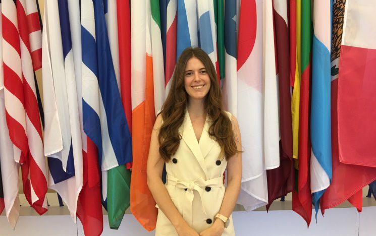 Sofia, an MA student in Corruption, sitting in front of some flags