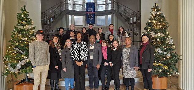 Group photo of people standing in front of stair case with Christmas trees either side of the group.