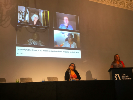 projection onto a wall shows 4 people on a Zoom call with the caption, 'general public there is so much confusion about missing periods and so on'. on women sits in front of the wall at a long panel table and one stands next to her behind a podium that reads 'The British Academy"