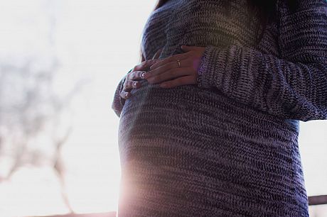 image of a pregnant person's baby bump, they are wearing a pink knitted jumper, and the sun is shining out from behind their bump