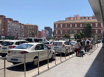 Photo of a line of taxis with people queuing for them.