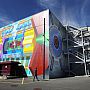 The outside of a concreate building with graffiti covering one wall depicting colorful scientific equipment