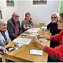 Image of a young person explaining the storytelling game to a group of four older people. They are sitting at a wooden table with photos on it.