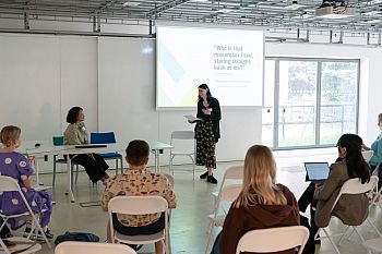  Person presenting to a group of people. Presentation slide with the text 'Who is that researcher I see, staring straight back at me?'