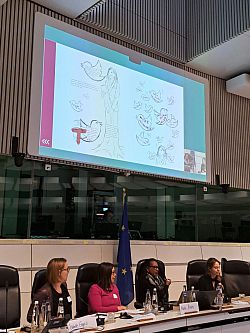 Dr Rebekka Kesberg  and others on a panel. PowerPoint presentation behind them has a commissioned artwork about the research.