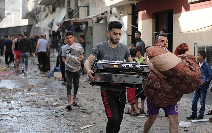 Two people walking through a street, carrying their belongings.