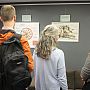 Group of people standing in front of and admiring artwork during the exhibition opening event