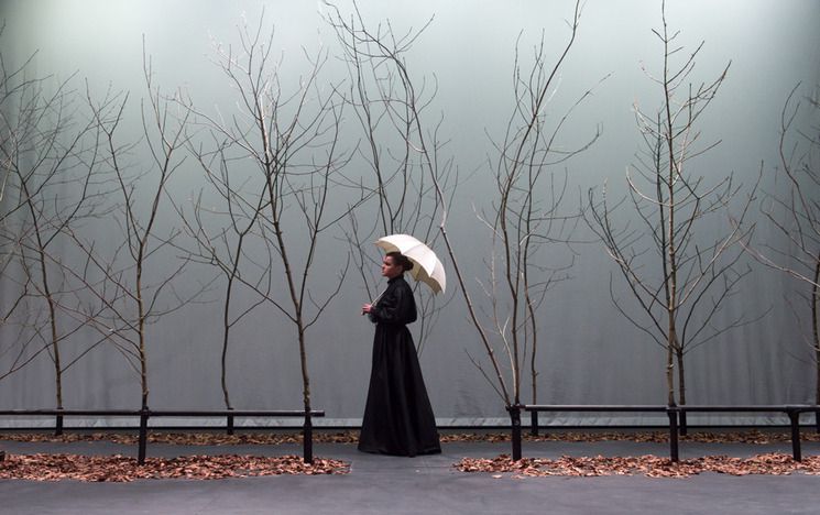 Woman in black dress walking through trees with white umbrella