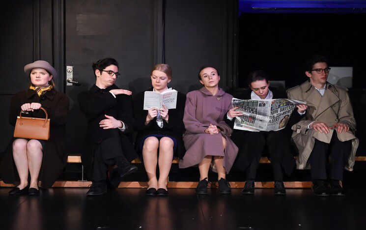 Six people sitting on a bench, some staring ahead, some reading book / newspaper