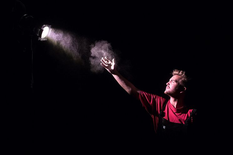 Male student reaching towards a theatre light