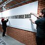 Three people positioning printed paper on a wall