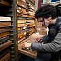 A man selects lettered pieces from a set of wooden drawers, for the printed press