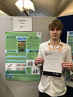 Elliot Jones standing in front of his academic poster, holding his certificate for attending Posters in Parliament 2025