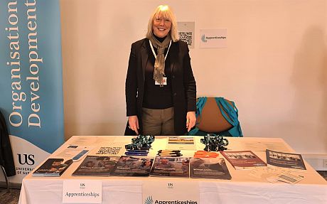Chris Hamilton standing behind a stall covered in apprenticeships promotional material