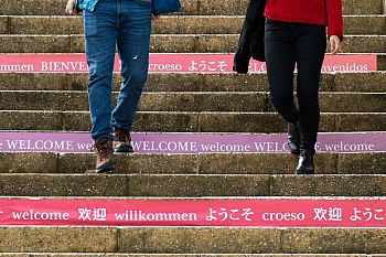 Two people walking down some concrete steps decorated with the word 'Welcome' in multiple languages