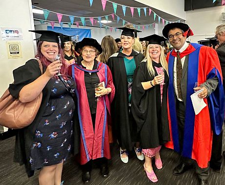 Two faculty in academic robes, plus several students in a room with bunting, to celebrate graduation