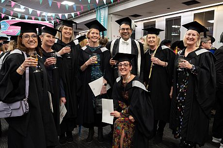 A faculty member in academic robes, plus several students in a room with bunting, to celebrate graduation