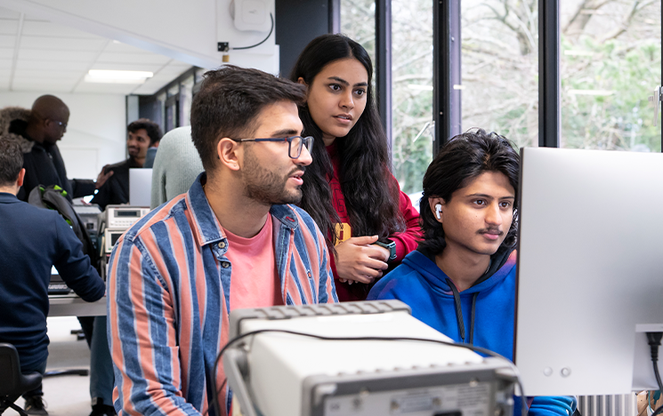 Three students gathered around a computer screen.