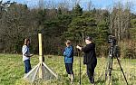 A man films two Nature Sense colleagues stood next to a monitoring station on Gravetye Estate