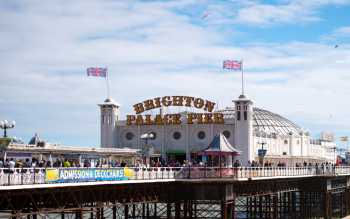 Brighton Pier taken from the seafront, with the bright sign in vision and people walking along it.