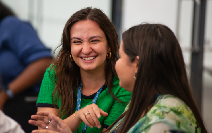 Two students sit together and smile, the image is a close up of their faces and they wear green T-shirts.