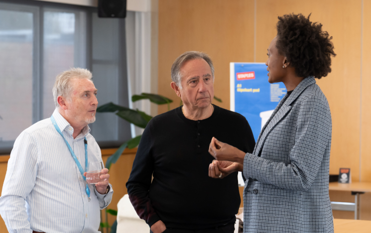 A business woman speaks and gestures with her hands as she speaks to two businessmen.