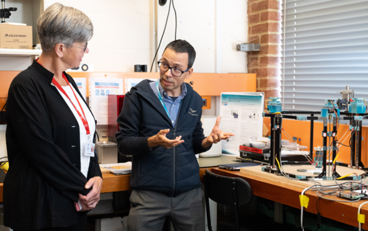 A lecturer talking to the Vice-Chancellor in a robotics lab.