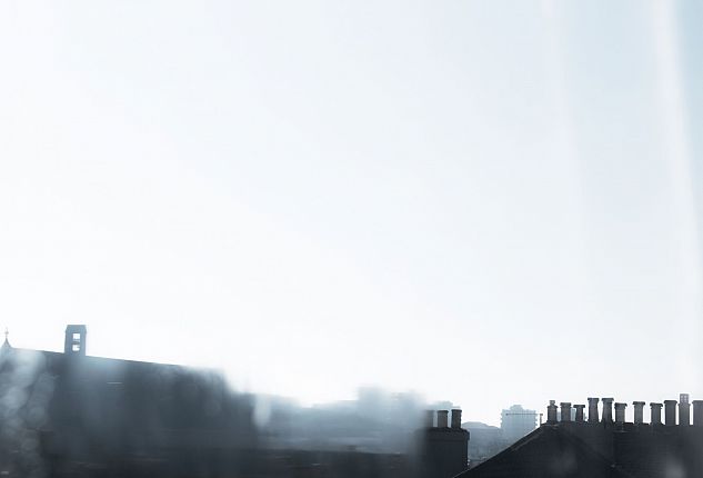 A blurry photograph with a rooftop, tall buildings in the distance and the sky